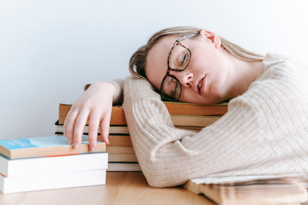 Tired female student sleeping on books in light room